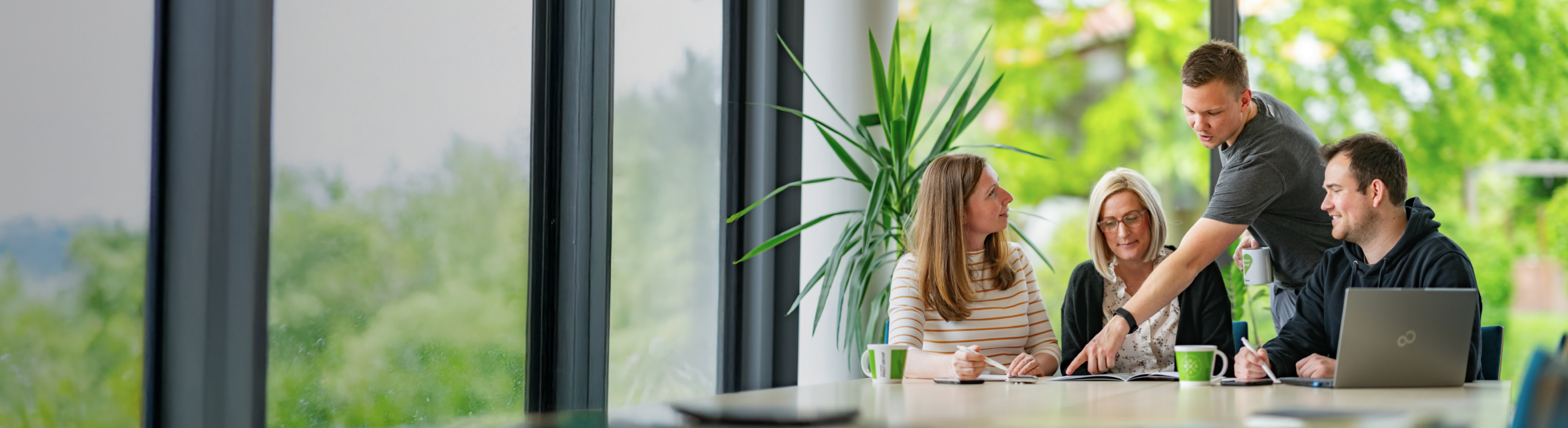 Personen sitzen an Meetingtisch und unterhalten sich in einem hellen Büro