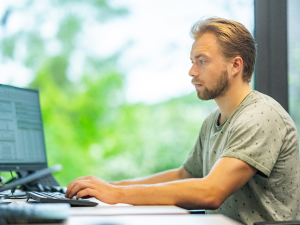 Mitarbeiter sitzt am Schreibtisch und schreibt etwas am PC